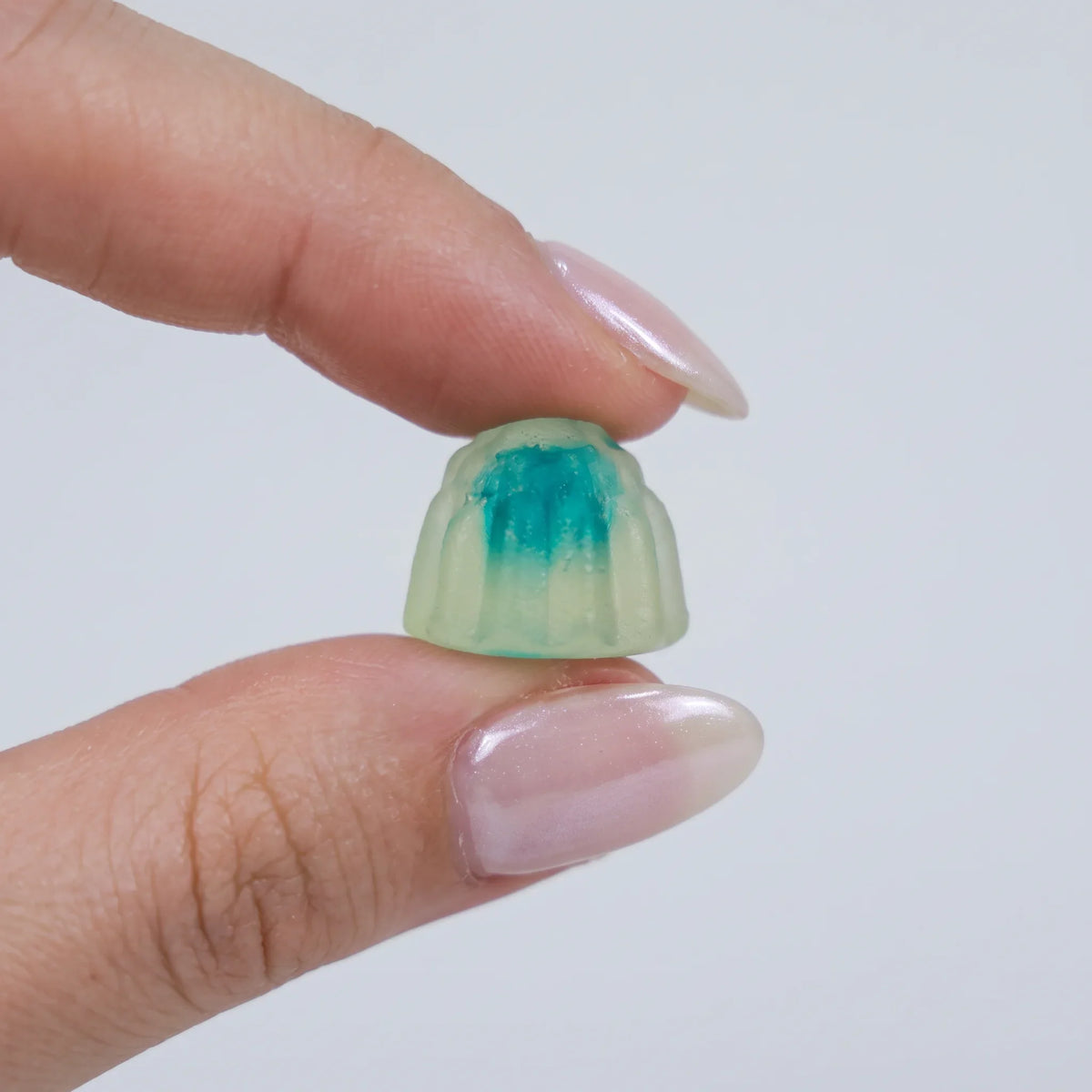 Goma de creatina Zelthy entre dois dedos, com o núcleo softgel turquesa visível
