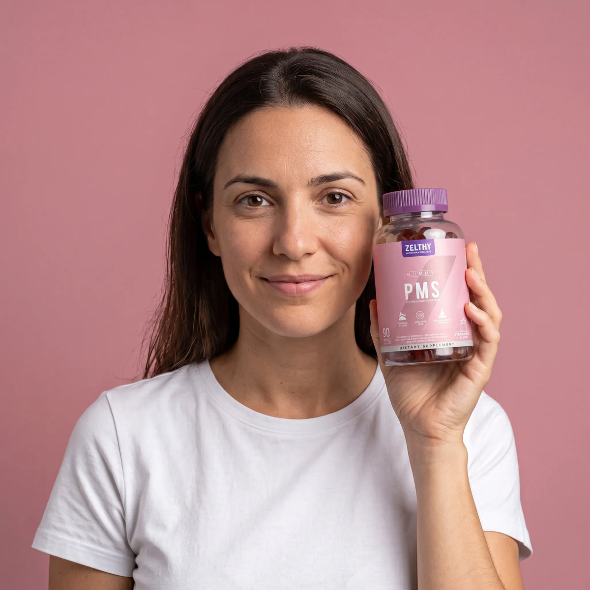 Mulher a segurar o frasco de gomas PMS Zelthy, em fundo rosa