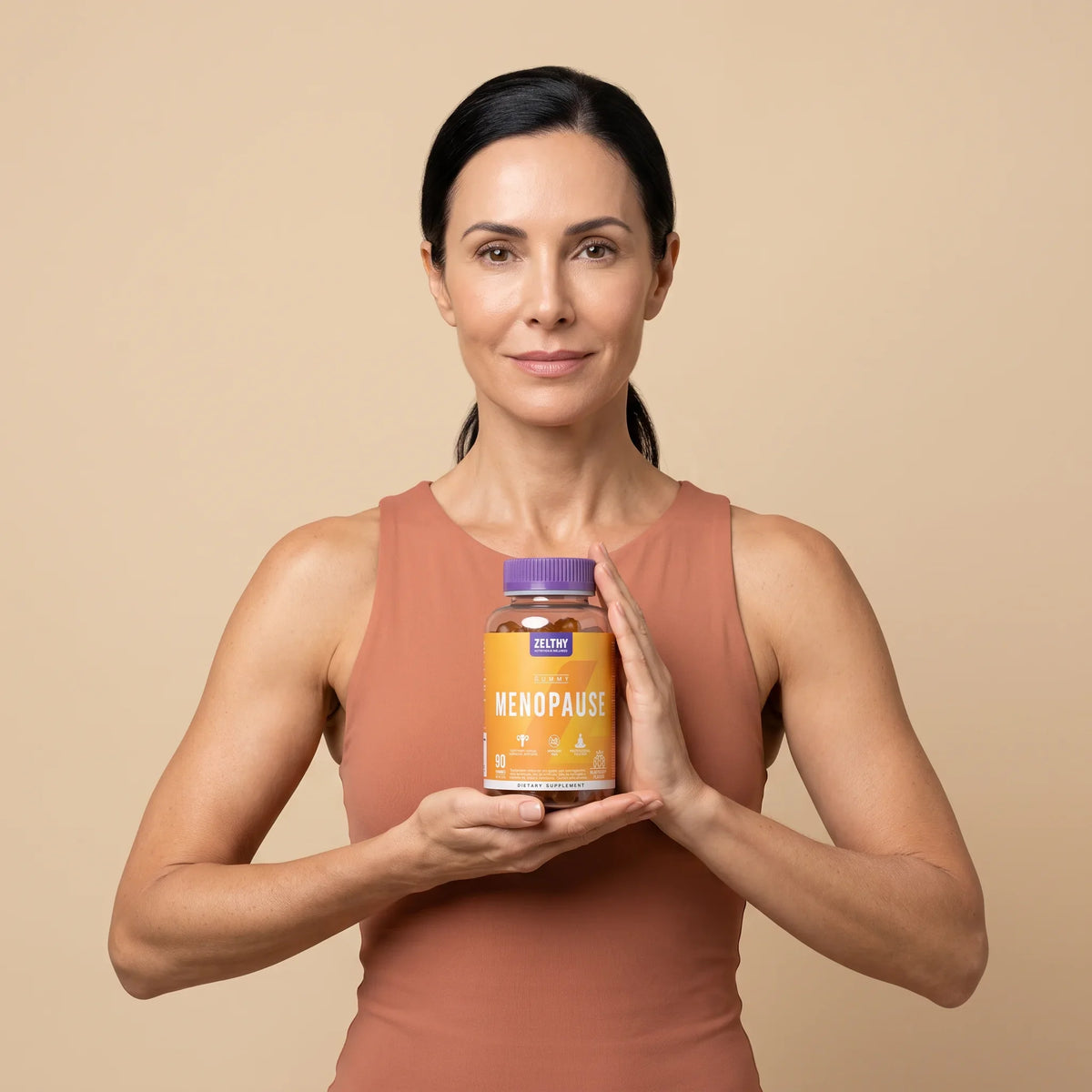 Mulher em top de treino a segurar o frasco de gomas Menopausa Zelthy